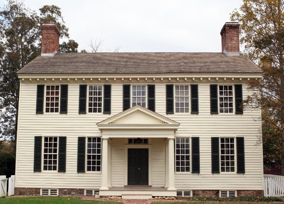 A symmetrical, two-story pale yellow clapboard house with a central columned portico and two brick chimneys